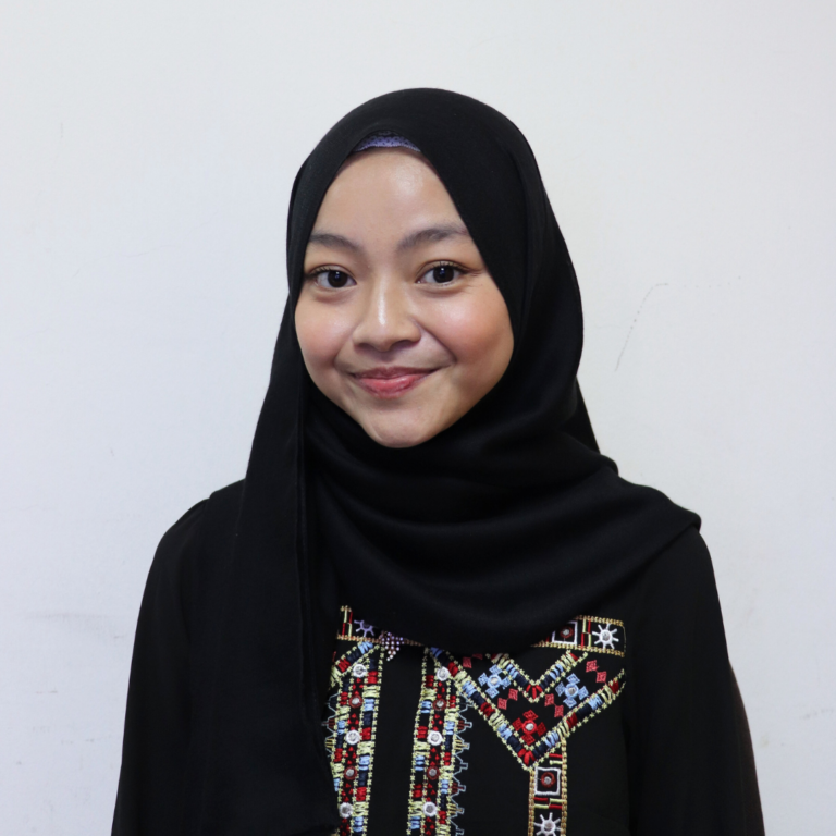 Young woman in black hijab, smiling, wearing traditional embroidered attire for cultural events.