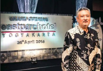 Modern hotel grand opening signage in Yogyakarta with a man in patterned shirt standing nearby.