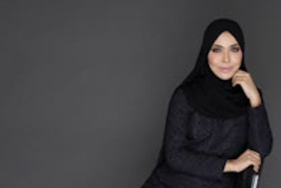 Modern Muslim woman wearing hijab and dark modest dress, smiling confidently.