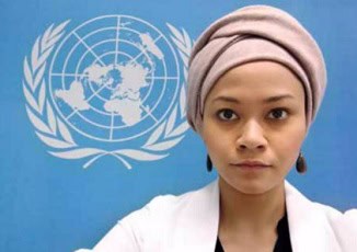 UN woman with headscarf in front of United Nations logo, diplomatic, international affairs, gender equality image.