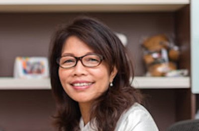 Experienced businesswoman smiling in an office setting with books and plants.
