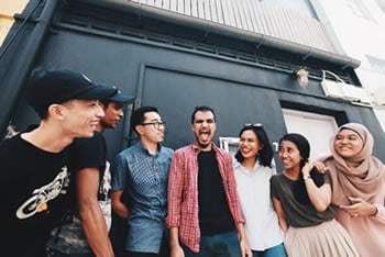 Diverse group of friends smiling outdoors near a building in casual clothing.