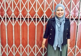 Vibrant woman wearing hijab smiling in front of colorful gate, celebrating RIMA event in style.